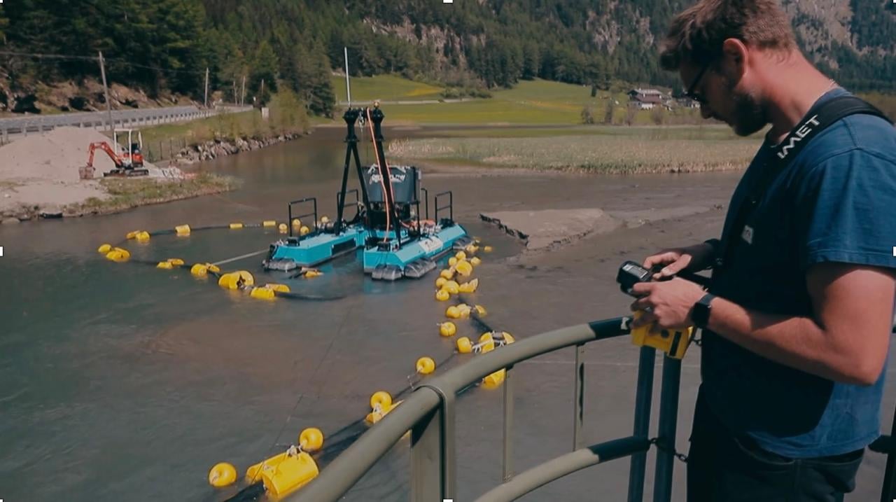 Operator controlling a dredge by remote from the dam wall, with the dredge working in the reservoir